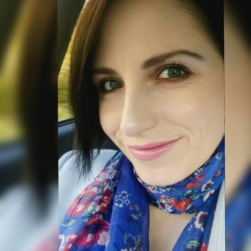 Portret uśmiechniętej kobiety z zielonymi oczami, w niebieskiej chuście w kwiaty, z delikatnym makijażem i ciemnymi włosami do ramion, zrobiony wewnątrz samochodu.