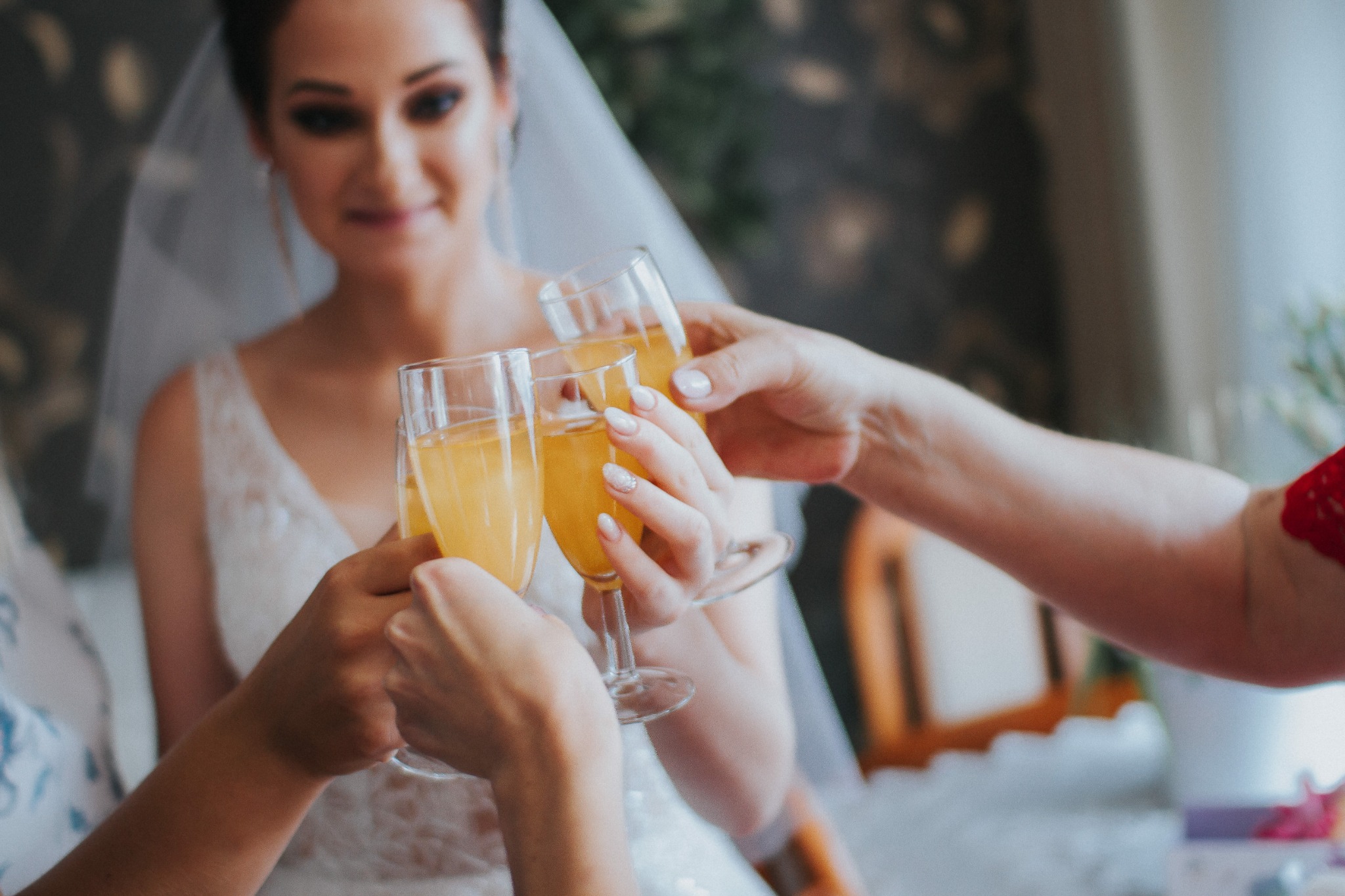 Panna młoda w białej sukni i welonie uśmiecha się, wznosząc toast z szampanem z dwiema osobami.