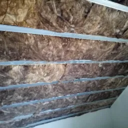 Izolacja z wełny mineralnej zamontowana między profilami metalowymi poddasza, widok od dołu.