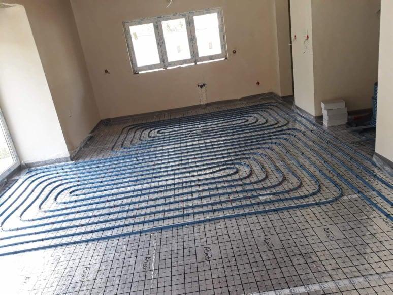 Niebieskie rury ogrzewania podłogowego ułożone na siatce z folią Altech w jasnym pomieszczeniu z oknem, przygotowane do zalania wylewką.