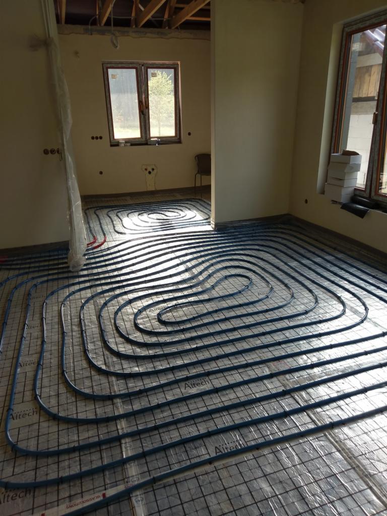 Instalacja ogrzewania podłogowego z rur Altech na folii z rastrem w surowym stanie, widoczne okna i niezakończone ściany.