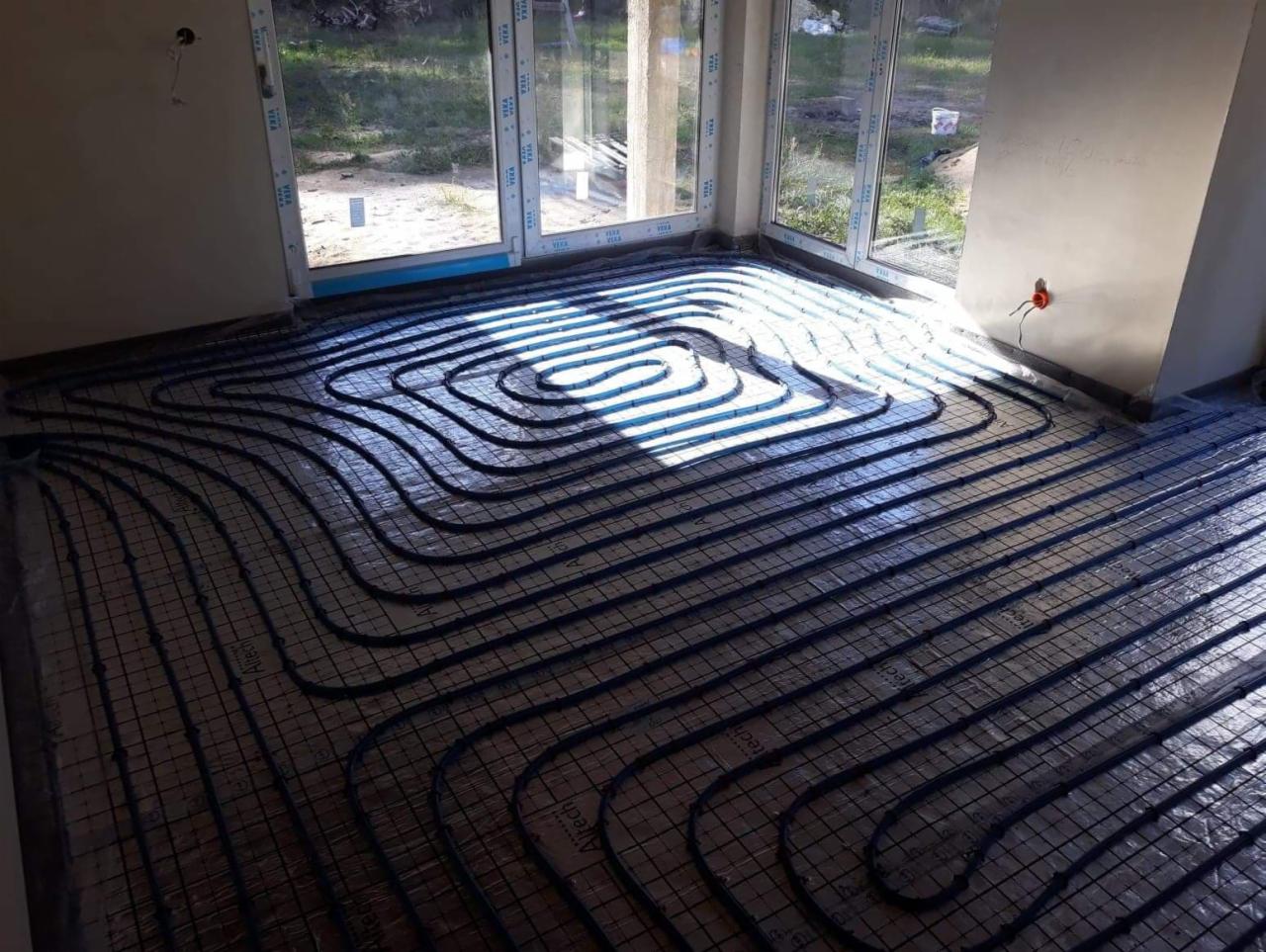 Instalacja ogrzewania podłogowego w nowym budynku, widoczne rury grzewcze ułożone na siatce montażowej, przygotowane do zalania wylewką.