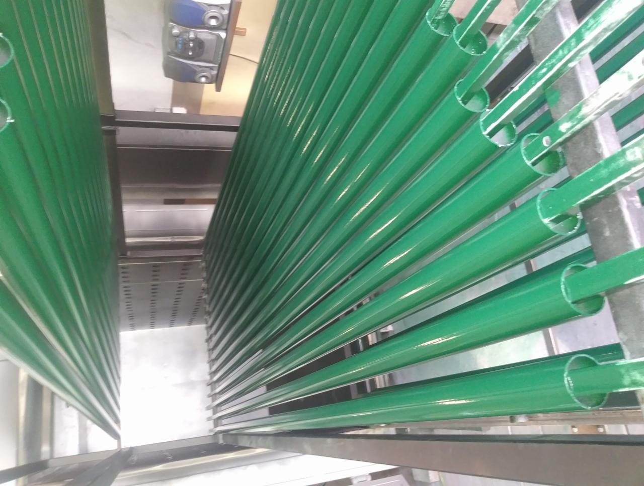 Rzędy zielonych, pomalowanych proszkowo, metalowych rur w trakcie procesu suszenia w piecu przemysłowym.