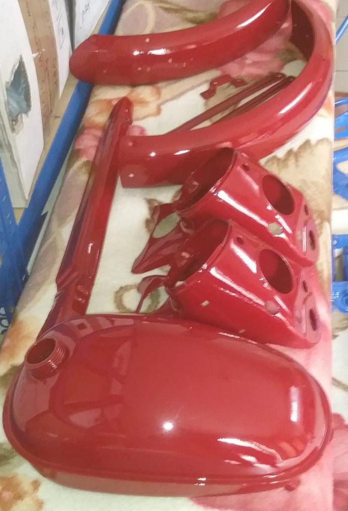 Czerwone, błyszczące elementy motocyklowe: błotniki, zbiornik paliwa i obudowy lamp, po renowacji lakierniczej, leżące na wzorzystej tkaninie.