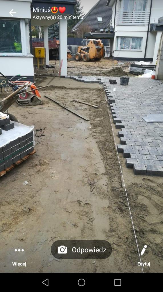 Układanie szarej kostki brukowej w Szczecinie, widoczny fragment ułożonej nawierzchni, paleta z kostką, ubijarka i miniładowarka w tle.