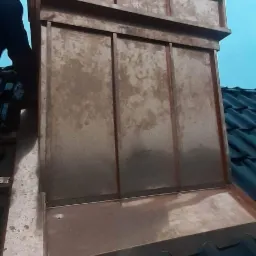 Nowa obróbka komina z blachy w kolorze miedzi, z widocznymi łączeniami i fakturą, na tle ciemnych dachówek i błękitnego nieba.