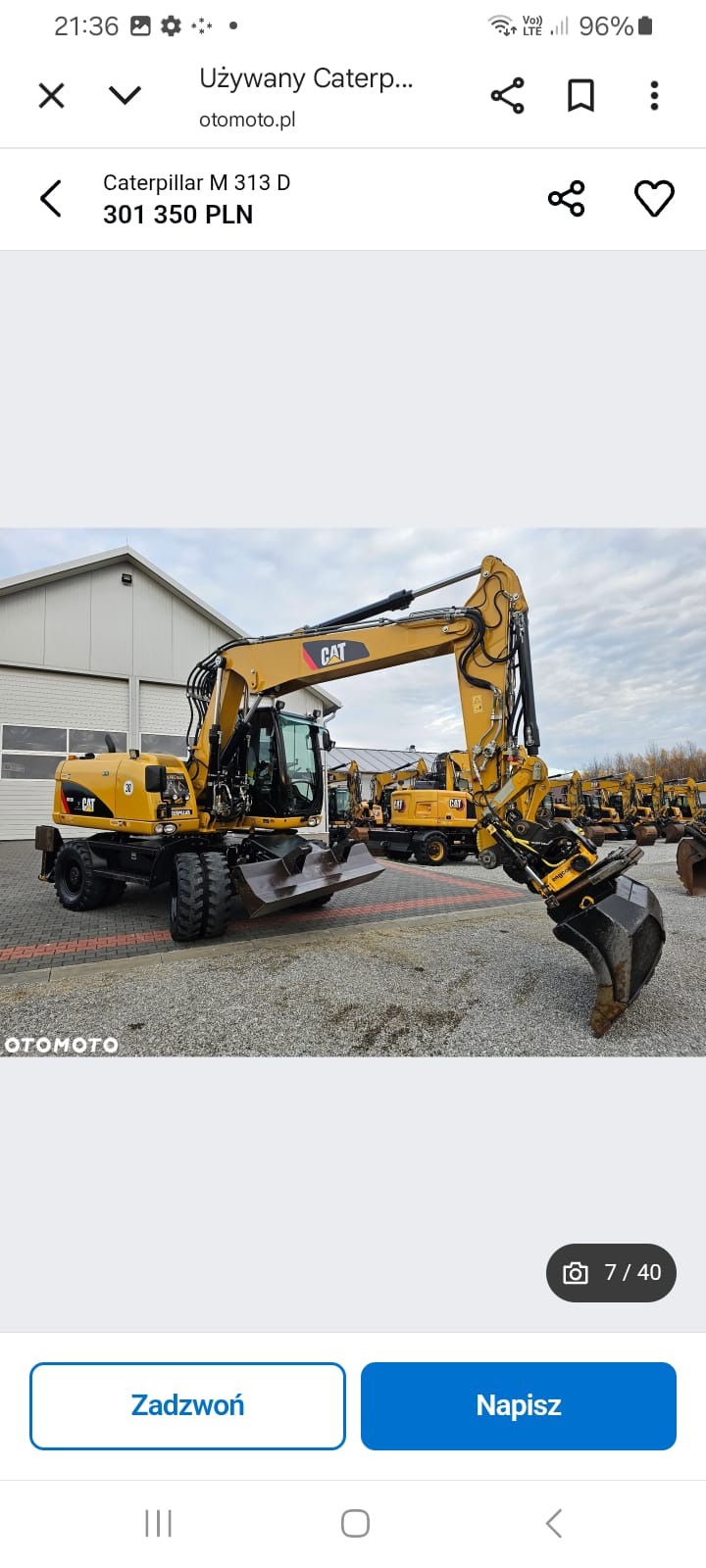 Żółta koparka kołowa Caterpillar M313D na placu z innymi maszynami. Widoczny budynek w tle. Ujęcie z boku, eksponujące ramię koparki i łyżkę.