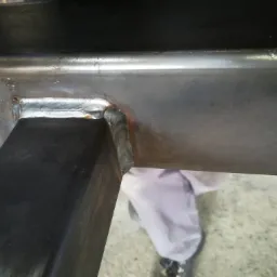 Spoina łącząca dwa metalowe profile, widoczne ślady po procesie spawania i krople wody na powierzchni metalu.