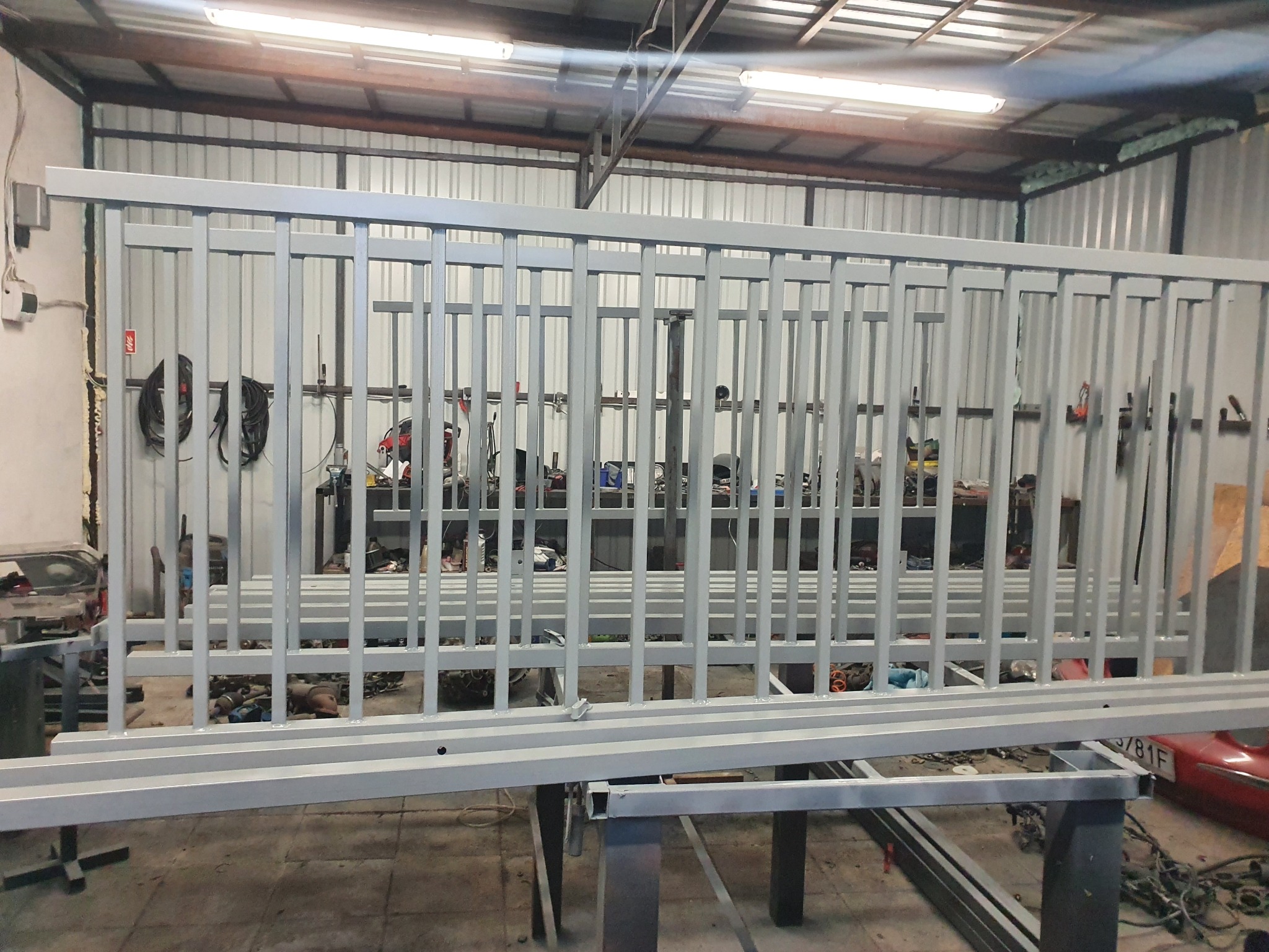 Pomaranczowa, pomalowana proszkowo balustrada stalowa z pionowymi prętami, spawana na metalowym stole warsztatowym w hali produkcyjnej.