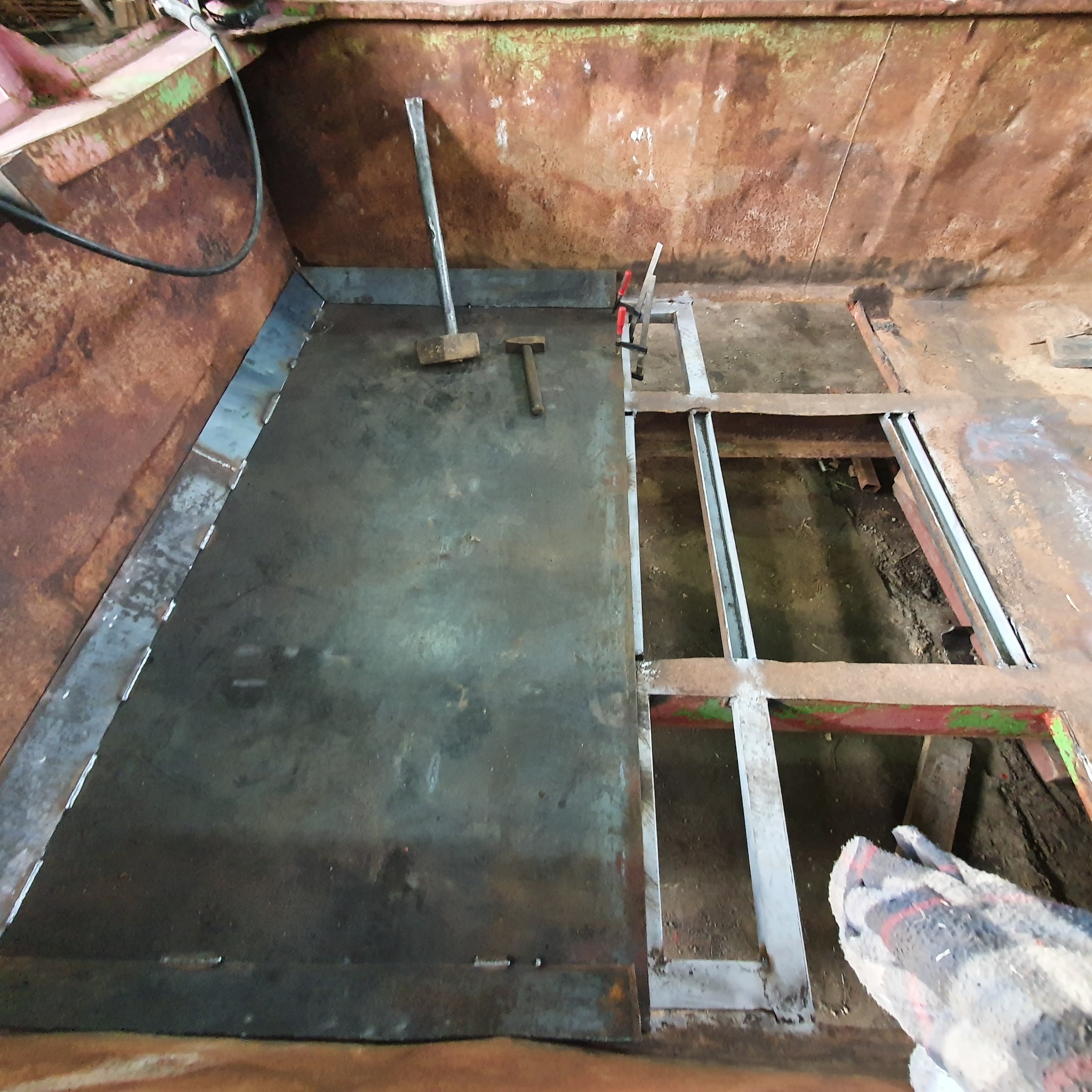 Wnętrze metalowej konstrukcji w trakcie naprawy: nowa blacha przyspawana do skorodowanych ścian, widoczne narzędzia - młotki i zaciski.