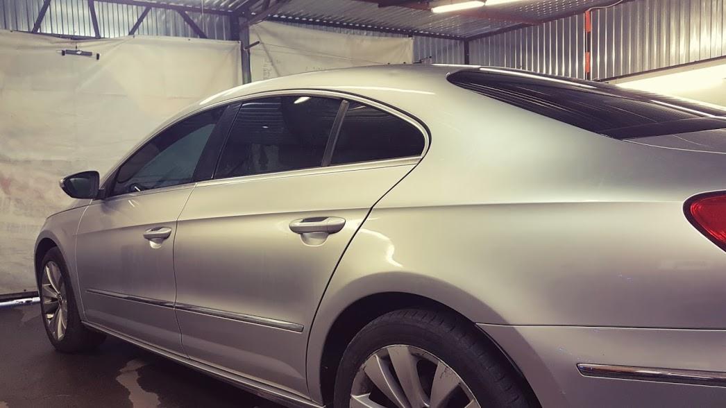 Srebrny samochód typu coupe z przyciemnionymi szybami bocznymi i tylną szybą, zaparkowany w warsztacie z widoczną konstrukcją sufitu.