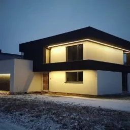 Nowoczesny, dwukondygnacyjny dom z płaskim dachem i podświetleniem LED, widoczny o zmierzchu, z delikatnym śniegiem na trawniku.