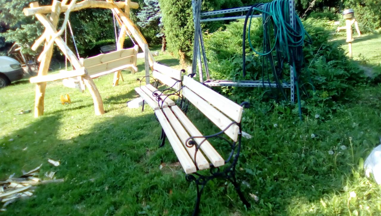 Dwie ławki ogrodowe: jedna klasyczna z metalowymi nogami i drewnianym siedziskiem, druga w formie huśtawki z gałęzi drzew, ustawione na trawniku w ogrodzie.