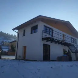 Nowoczesny, ocieplony dom jednorodzinny z zewnętrznymi schodami w zimowej scenerii, widoczny pracownik w czarnej bluzie.