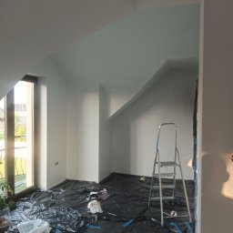 Mardosz - Poddasze z ukośnymi ścianami, świeżo pomalowane na biało, podłoga zabezpieczona czarną folią. Przy oknie z widokiem na balkon stoi aluminiowa drabina.