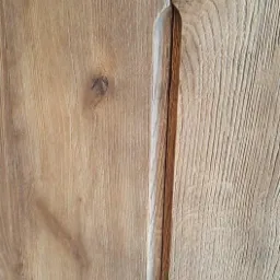 Detal rustykalnych drzwi szafy z litego drewna z wpuszczonym podłużnym uchwytem.