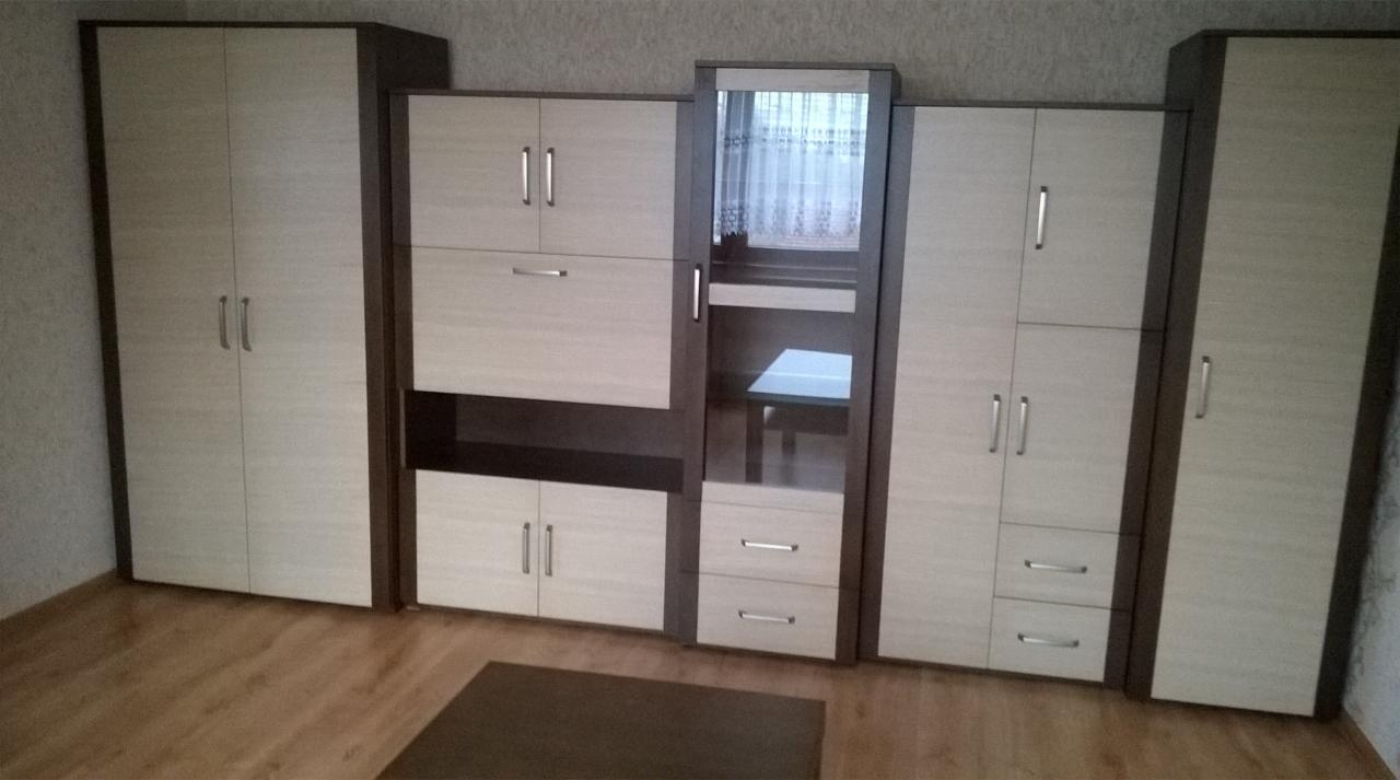 Zestaw mebli pokojowych z jasnego drewna z ciemnymi obramowaniami, składający się z szaf, szafek i toaletki z lustrem, ustawiony na drewnianej podłodze.