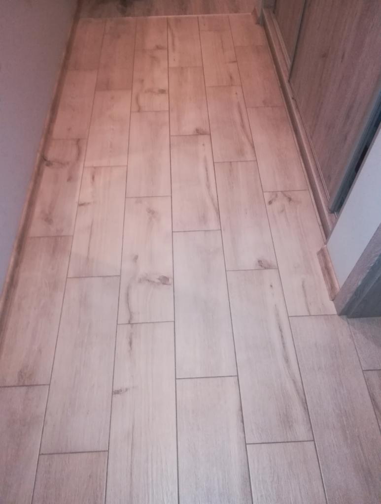 Ułożona podłoga z paneli imitujących drewno, widok z góry, fuga w kolorze szarym, ściana pomalowana na szaro, widoczne drzwi przesuwne do szafy.