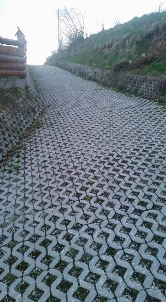 Podjazd z ażurowych płyt betonowych na wzniesieniu, z widoczną skarpą porośniętą trawą i drewnianym ogrodzeniem po bokach.