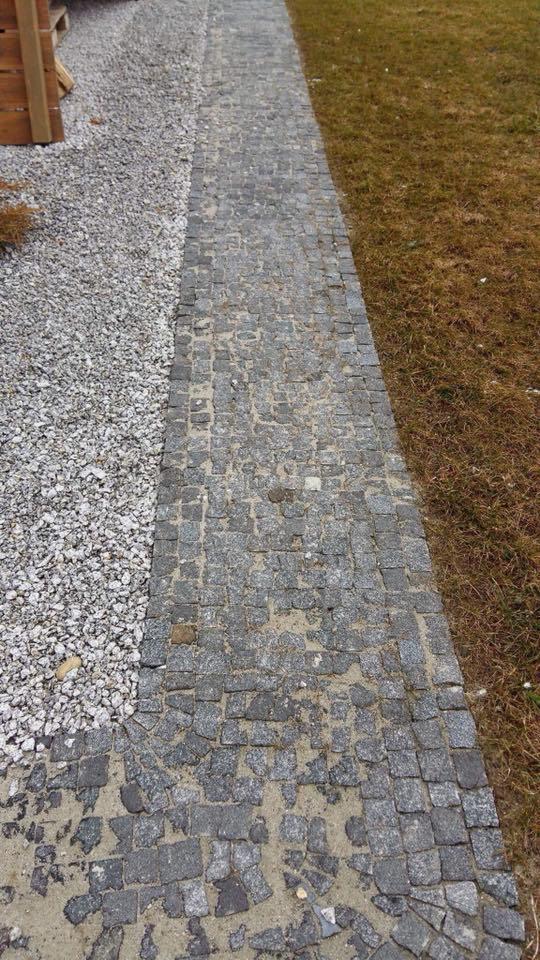 Ścieżka z szarej kostki granitowej, obok wysypany żwir i trawa, widok z góry.