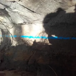 Wykop z zaznaczoną niebieską linią przebiegu instalacji, widoczne ślady po wykopie i cień gałęzi.