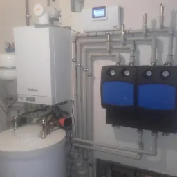 Nowoczesny system grzewczy z kotłem Viessmann, zasobnikiem ciepłej wody i rozdzielaczem z manometrami, instalacja w pomieszczeniu technicznym.