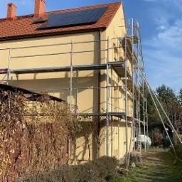 Dom we Wrocławiu w trakcie prac elewacyjnych, widoczne rusztowania i panele słoneczne na dachu.