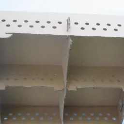 Kartonowe pudło transportowe z przegródkami i otworami wentylacyjnymi, przeznaczone do transportu piskląt, ustawione na białym podłożu.