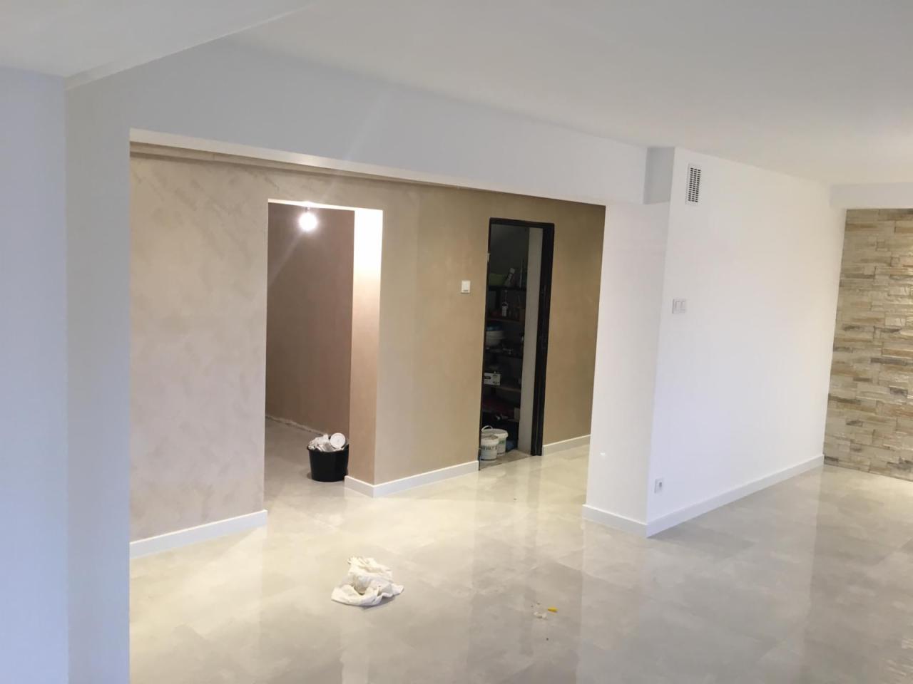 Wykończone wnętrze z efektem dekoracyjnej szpachli na ścianach, widoczne fragmenty podłogi z połyskiem i dekoracyjny panel ścienny z kamienia.