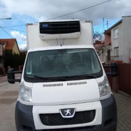 Biały samochód dostawczy z chłodnią Carrier, zaparkowany na ulicy z kostki brukowej, widok z przodu, tablica rejestracyjna FSU 26968.