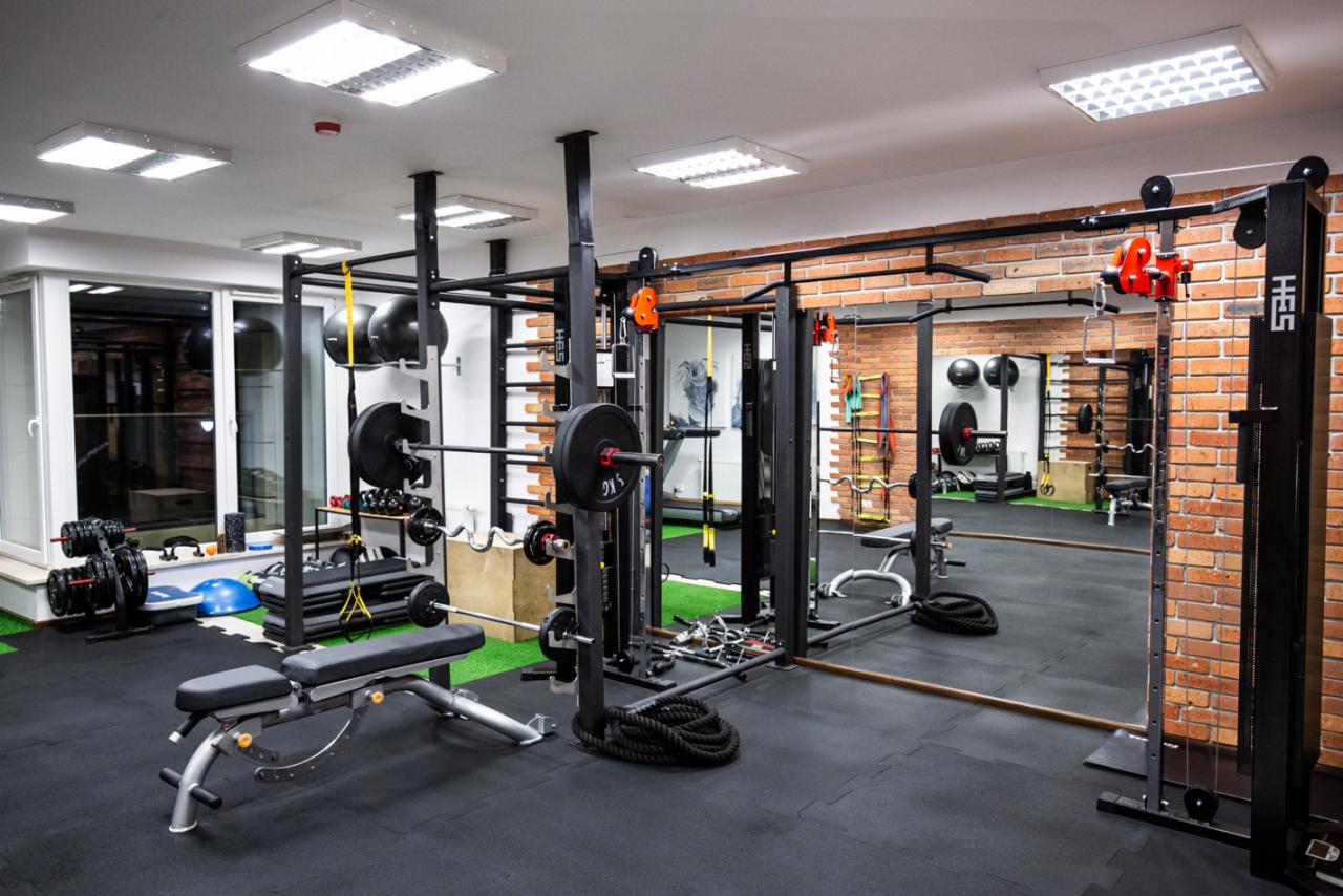 Profesjonalna siłownia z czarną podłogą, sztuczną trawą, sprzętem do ćwiczeń siłowych, lustrami i ścianą z cegły.