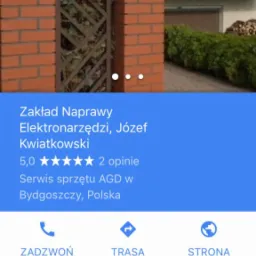 Fasada budynku z szyldem 'ELEKTRO-NARZĘDZI' widoczna za ceglanym ogrodzeniem i ozdobną metalową bramką.