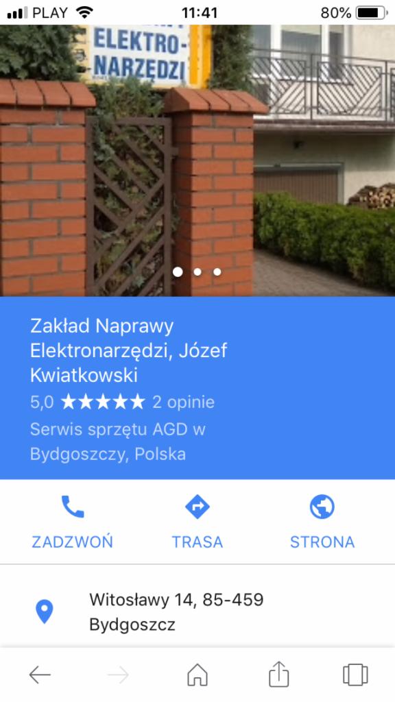 Fasada budynku z szyldem 'ELEKTRO-NARZĘDZI' widoczna za ceglanym ogrodzeniem i ozdobną metalową bramką.