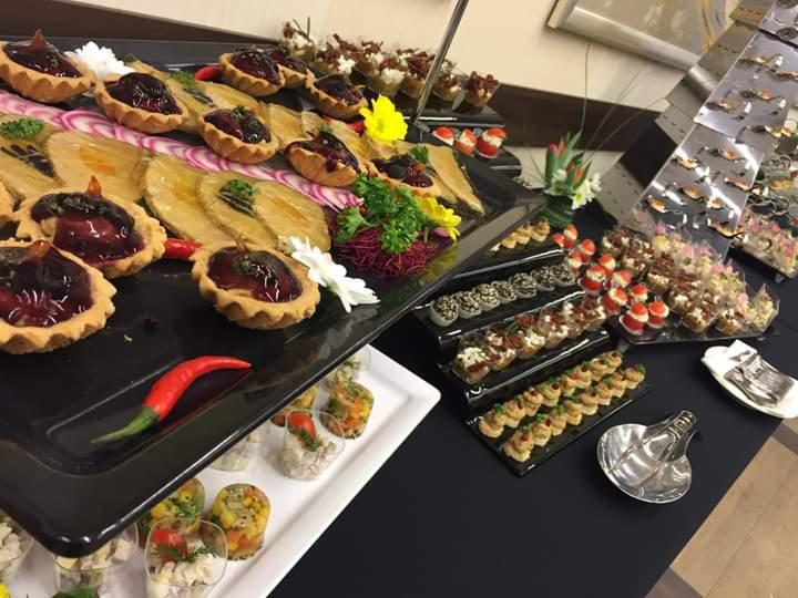 Zestaw różnorodnych przekąsek na czarnych i białych tacach, w tym tartaletki z ciemnym nadzieniem, roladki z warzywami w przezroczystych kubeczkach, kanapeczki i inne finger food, udekorowane...