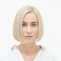 Portret kobiety z krótkimi, platynowymi włosami, ubranej w białą koszulę, na jasnym tle.