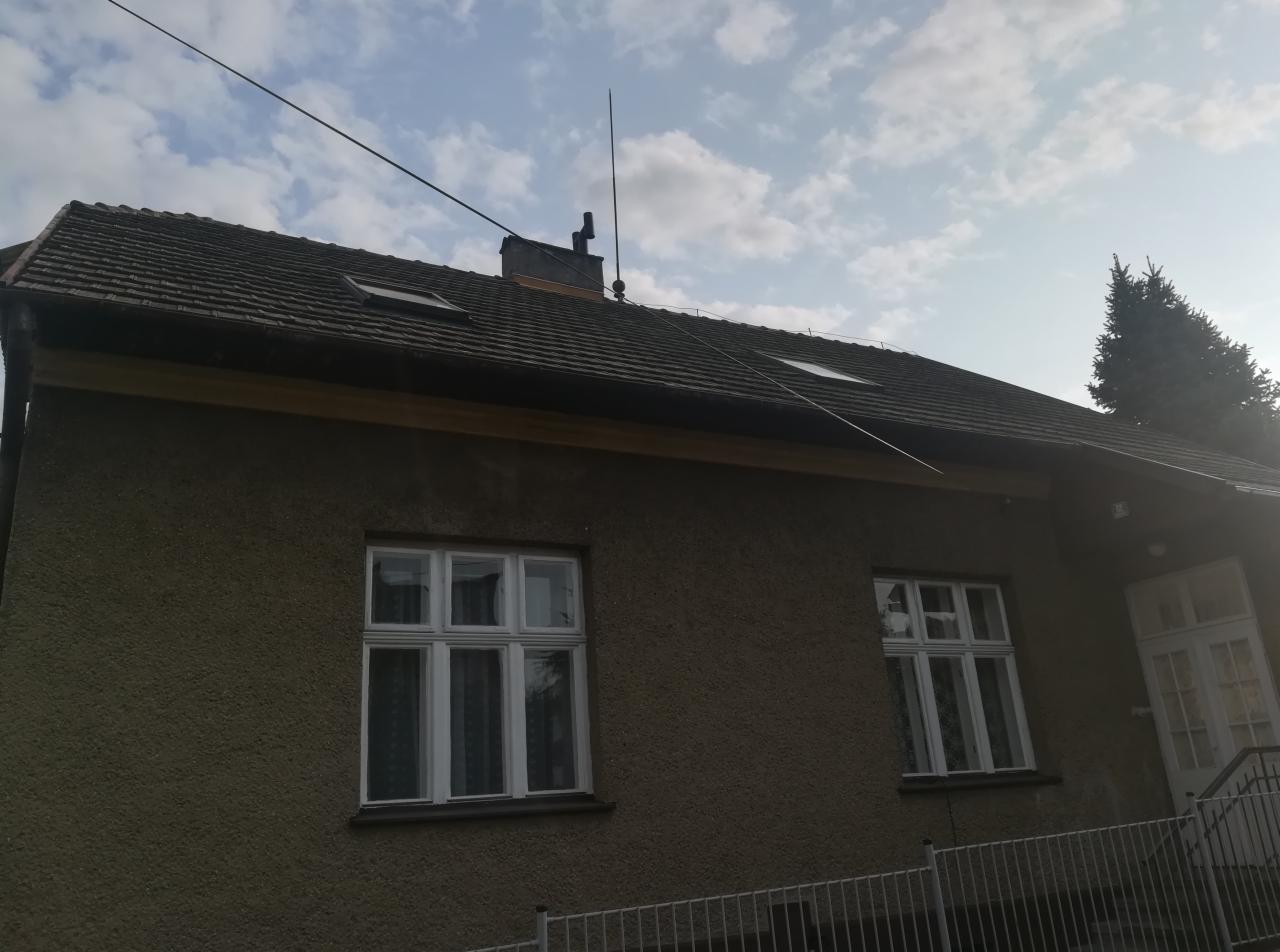 Dom jednorodzinny z szarą elewacją i dachem z dachówki ceramicznej, widoczne okna dachowe, instalacja odgromowa, rynny i komin.