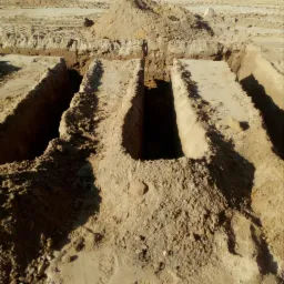 Wykopane rowy w piaszczystym terenie, prawdopodobnie pod fundamenty lub instalacje, z pryzmą ziemi w tle.
