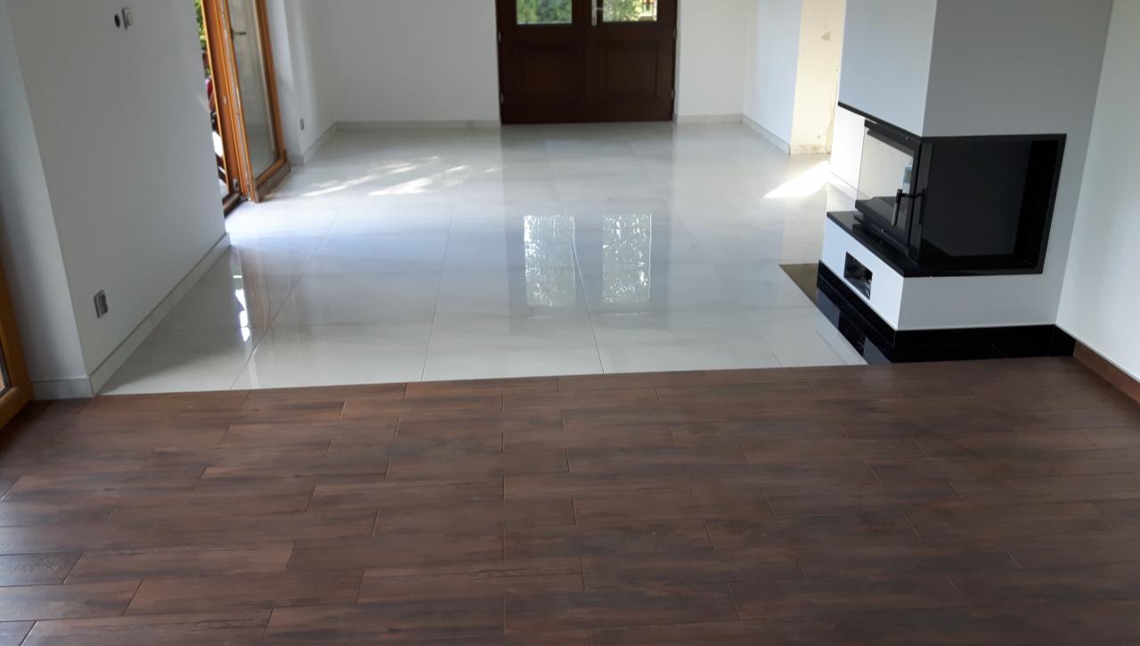 Salon z dwoma rodzajami podłóg: błyszczące, jasne płytki ceramiczne oraz ciemne panele drewnopodobne, z nowoczesnym kominkiem narożnym.