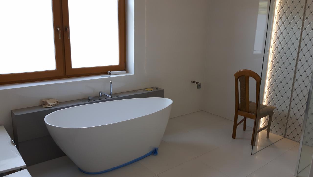 Nowoczesna, wolnostojąca wanna owalna z baterią podtynkową, osadzona na podwyższeniu, zabezpieczona niebieską folią ochronną, w minimalistycznej łazience z drewnianym oknem i krzesłem obok kabiny...