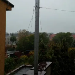 Metalowy komin wentylacyjny z daszkiem na dachu budynku, widok z góry w pochmurny dzień.