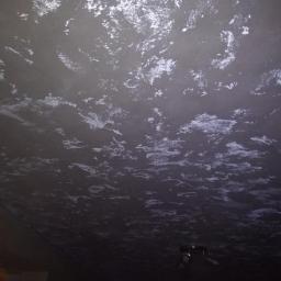 S.S.bud - Sufit w ciemnym odcieniu szarości z nieregularnymi, jasnymi smugami, przypominającymi efekt dekoracyjny lub niedokładne położenie gładzi, widoczny fragment lampy sufitowej i drzwi.