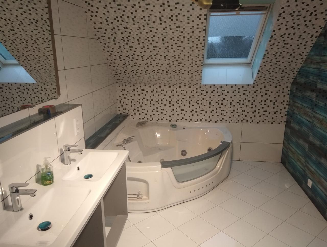 Wykończona łazienka na poddaszu z wanną z hydromasażem, dwiema umywalkami nablatowymi i mozaiką na ścianach.