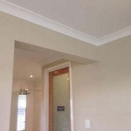 ORKAN Paweł Warpas - Świeżo pomalowane wnętrze z listwami przypodłogowymi i widoczną kabiną prysznicową w tle, neutralna kolorystyka ścian.