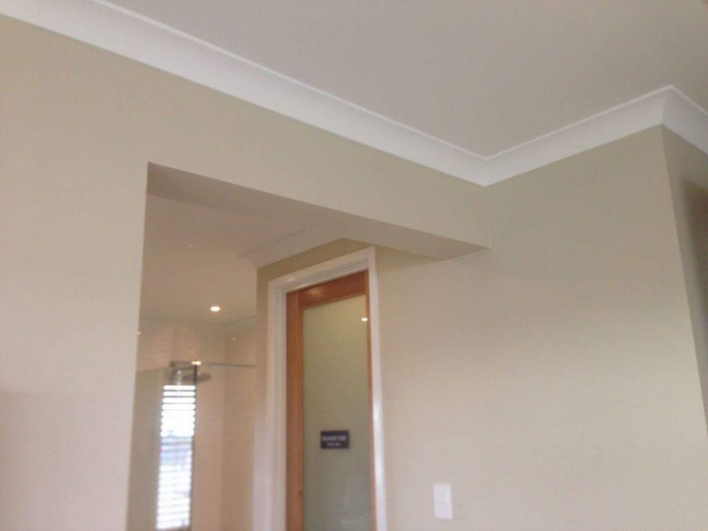 Świeżo pomalowane wnętrze z listwami przypodłogowymi i widoczną kabiną prysznicową w tle, neutralna kolorystyka ścian.