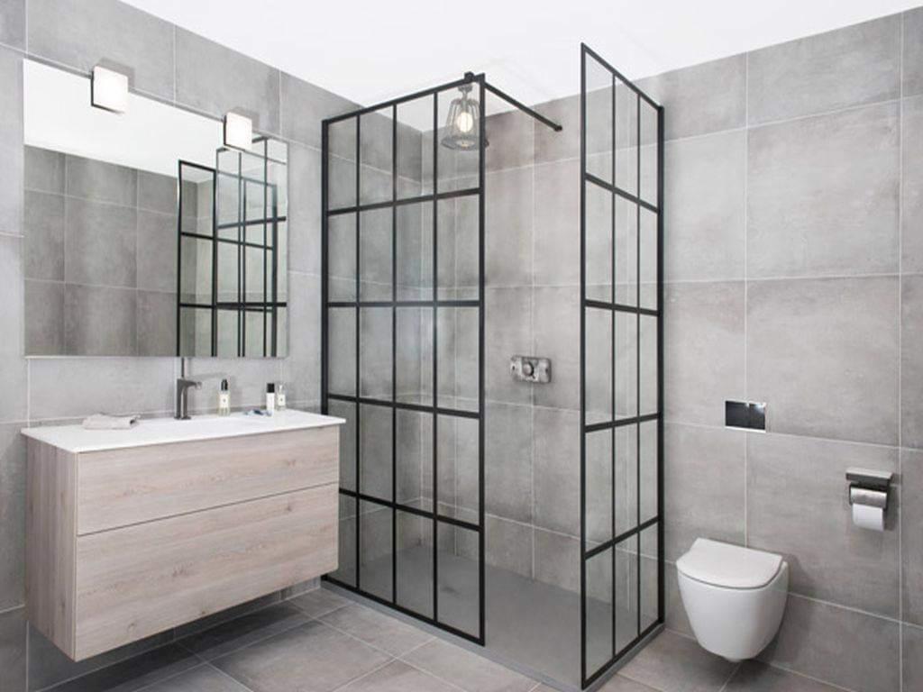 Nowoczesna łazienka w szarościach z kabiną prysznicową typu walk-in z czarnymi profilami, wiszącą toaletą i szafką pod umywalkę z jasnego drewna.