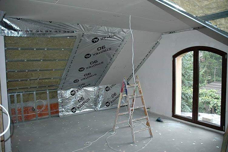 Poddasze w trakcie adaptacji: widoczne ocieplenie wełną mineralną, folia paroizolacyjna Strotext AL 90, metalowy stelaż pod płyty gipsowo-kartonowe oraz drewniana drabina oparta o ścianę przy oknie.