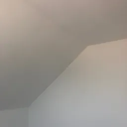 Świeżo pomalowane, białe ściany i sufit pod skosem w pokoju na poddaszu, widok z dołu.