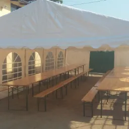 Wnętrze białego namiotu imprezowego z drewnianymi stołami i ławkami, widok z zewnątrz w słoneczny dzień.