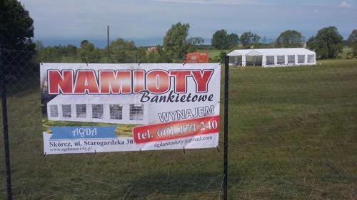 Baner reklamowy z napisem 'Namioty Bankietowe WYNAJEM' i numerem telefonu, w tle rozstawiony biały namiot bankietowy na zielonej łące.
