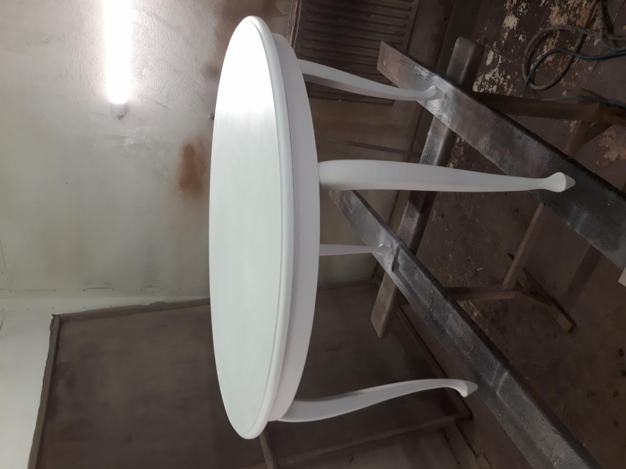 Okrągły stół na drewnianym stojaku, pomalowany świeżą, białą farbą, widoczne ślady farby na stojaku.